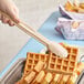 A person using Cambro beige plastic tongs to serve waffles at a hotel buffet.