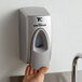 A person using a Rubbermaid Metallic Gray Manual Spray Soap Dispenser.