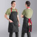A man wearing a black Uncommon Chef apron with red straps.