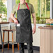 A man wearing a black Uncommon Chef Rebel bib apron with red webbing standing in a professional kitchen.