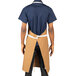 A man wearing a tan Uncommon Chef Rebel apron with natural webbing and three pockets.
