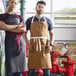 A man and woman wearing Uncommon Chef caramel aprons with natural webbing standing in a restaurant.