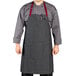 A man wearing a Uncommon Chef pinstripe denim bib apron with burgundy accents and 3 red pockets.