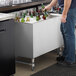 A man standing at a counter with a Regency stainless steel beer cooler and putting bottles in it.