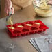 A person pouring batter into a red silicone heart mold.