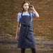 A woman wearing a Uncommon Chef denim apron with black webbing over a blue shirt.