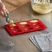 A person pouring liquid into a red Thunder Group Madeleine mold.