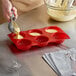 A person pouring batter into a red silicone Thunder Group dahlia mold.