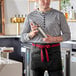 A black poly-cotton waist apron with red webbing, three pockets, and a front tie, measuring 14 by 30 inches.