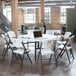 A white Lifetime round folding table with a laptop on it next to a white folding chair.