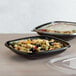 A Fineline black plastic bowl filled with pasta and olives on a table with another bowl of pasta and olives.