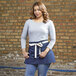 A woman wearing a Uncommon Chef navy waist apron with natural webbing over blue pants.
