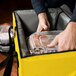 A person using a Sterno yellow insulated food carrier to hold a plastic container of food.