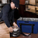 A man carrying a royal blue and silver Sterno insulated food delivery bag with a black strap.