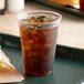 A Fabri-Kal plastic cup filled with a brown drink and ice on a tray.