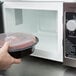 A person using a Panasonic commercial microwave to heat food in a plastic container with a lid.