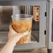 A hand holding a Choice translucent plastic deli container of soup.