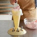 A cream colored pastry bag holder with metal tips holding a cream colored pastry bag with pink frosting.