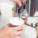 A person using a Vollrath Maximillian steel coffee urn to pour coffee into a cup.