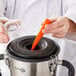 A person using a spoon to stir a smoothie in a clear glass cup on a counter.