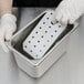 A person in white gloves holding a Vollrath stainless steel false bottom for a steam table pan.