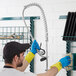 A man wearing blue gloves using a 1.15 GPM Pre-Rinse Spray Valve to clean a sink in a professional kitchen.