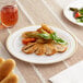 A Visions white plastic plate with gold bands holding food on a table with a glass of brown liquid.