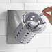 A hand holding a spoon in a Steril-Sil stainless steel flatware organizer with a gray perforated cylinder.