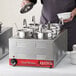 A man using an Avantco countertop food warmer to pour food into a pot.