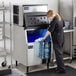 A woman in a black shirt standing in a school kitchen pouring water into an Avantco air cooled ice machine.