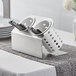 A Steril-Sil stainless steel flatware organizer with white perforated plastic cylinders holding utensils.