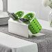 A silver Steril-Sil flatware organizer with lime green plastic cylinders holding silverware on a table in a home kitchen.