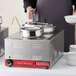 A man using an Avantco countertop food warmer to cook food in a large pot.