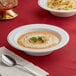 A Visions white plastic bowl filled with soup and a spoon on a table.