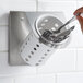 A hand placing a spoon in a Steril-Sil stainless steel flatware organizer with a white plastic cylinder.