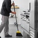 A man using a Rubbermaid jumbo broom with a black handle to sweep a floor in a professional kitchen.