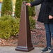 A woman standing next to a Rubbermaid brown cigarette receptacle.