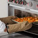 A person in San Jamar Bestan non-stick oven mitts putting food into an oven.