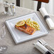 A Visions white plastic plate with silver bands holding a plate of food with a lemon slice on top.