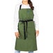 A woman wearing a sea green Uncommon Chef Aura bib apron with black webbing.