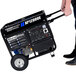 A man pushing a DuroMax portable gasoline powered generator with wheel kit.