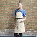 A woman wearing an ivory Uncommon Chef canvas apron with black webbing and pockets.