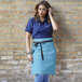 A woman wearing a blue Uncommon Chef waist apron standing in a professional kitchen.