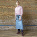 A man wearing a blue and gray Uncommon Chef Muse Bistro Apron with black webbing.