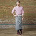 A man wearing a pink shirt and a gray Uncommon Chef bistro apron.