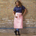 A woman wearing a coral pink Uncommon Chef bistro apron with natural webbing.