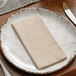 A white plate with a Hoffmaster Linen-Like Natural Kraft dinner napkin on it.