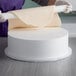 A person rolling out a white cylinder of dough on a wood surface.