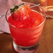 A strawberry cocktail with a red shimmer on a table in a cocktail bar.