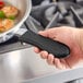 A hand using a San Jamar black silicone handle holder to hold a pan over food.